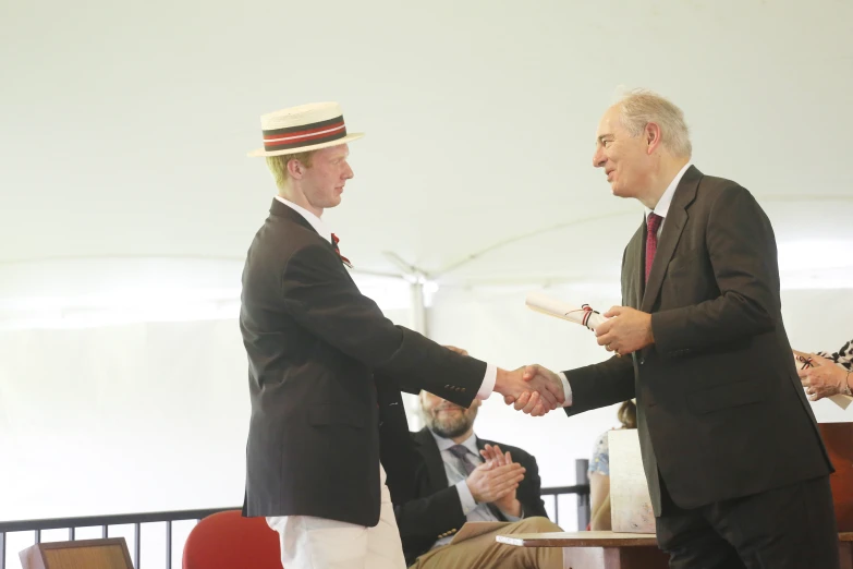 two men shaking hands during a function with the other men standing behind them