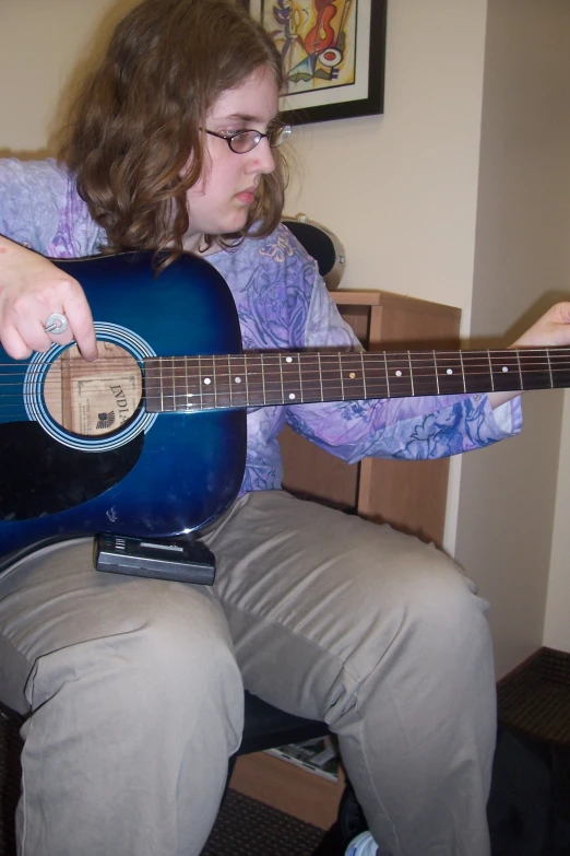 a girl wearing glasses playing a guitar and sitting down