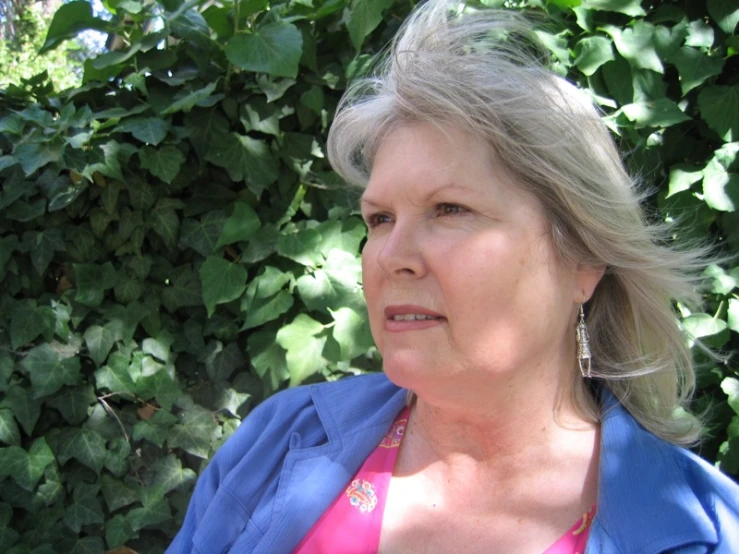 an older woman is posing for a picture in front of some greenery