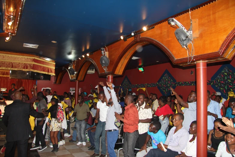 a group of people singing with their hands up in a large room with ceiling lights