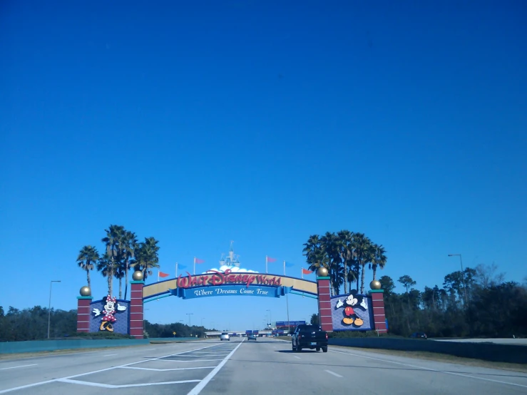 cars driving underneath a very tall colorful sign