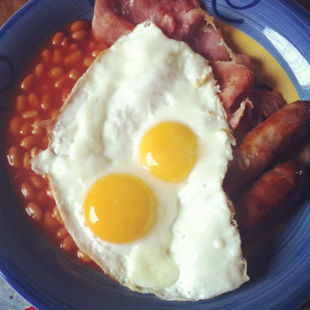 two fried eggs on a plate with beans and ham