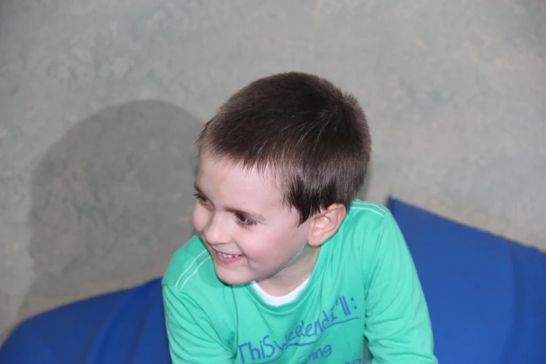 the little boy is smiling and sitting on the blue mat