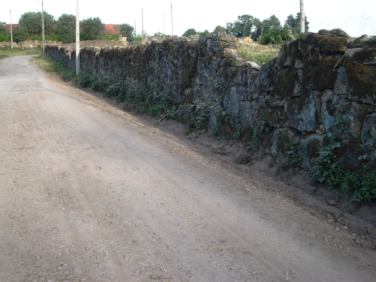 a stone fence is built into the side of a dirt road