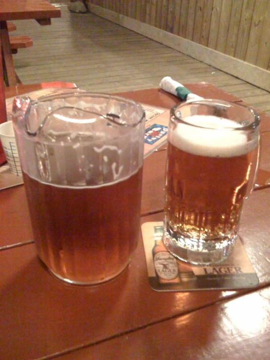 a large glass of beer next to a giant mug of beer