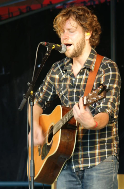 a man singing into a microphone while holding an acoustic guitar