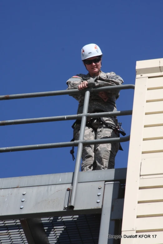 a male in military fatigues leaning on a metal rail with safety equipment