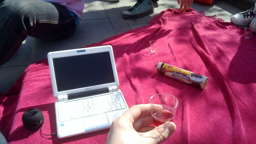 someone holding a glass near a laptop on a bed