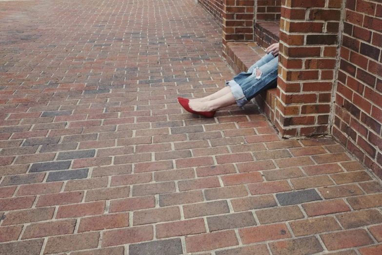 a woman with blue jean shorts and red shoes sitting on a brick walkway