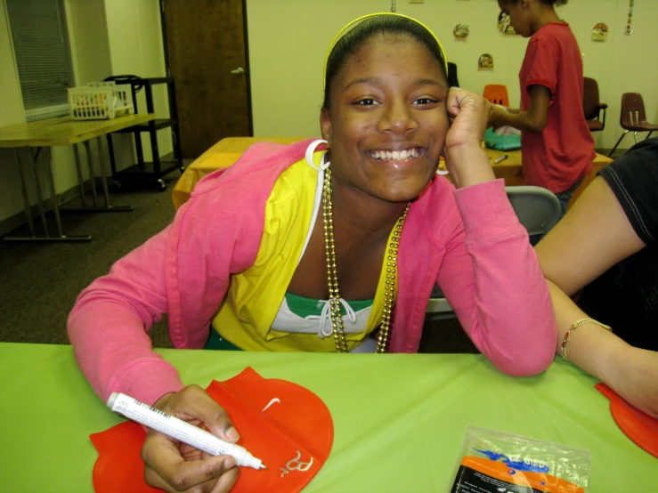 a girl sitting at a table holding a cell phone and smiling