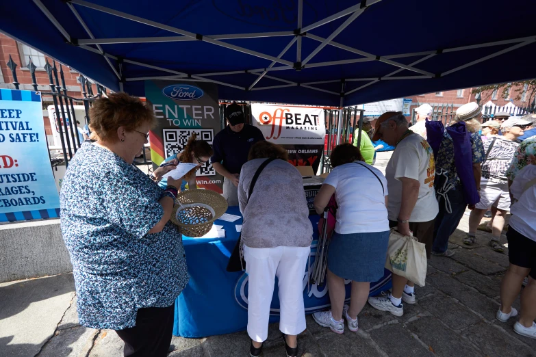 many people standing around a table under a blue tent