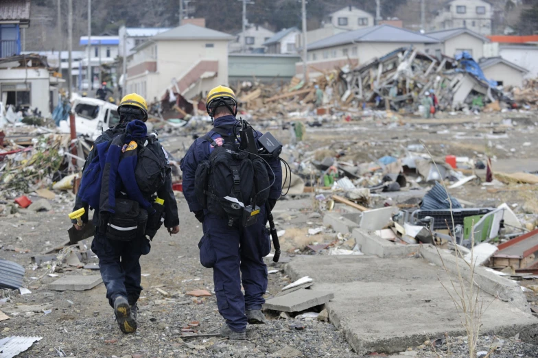 two firefighters walk among debris in the destroyed suburbs