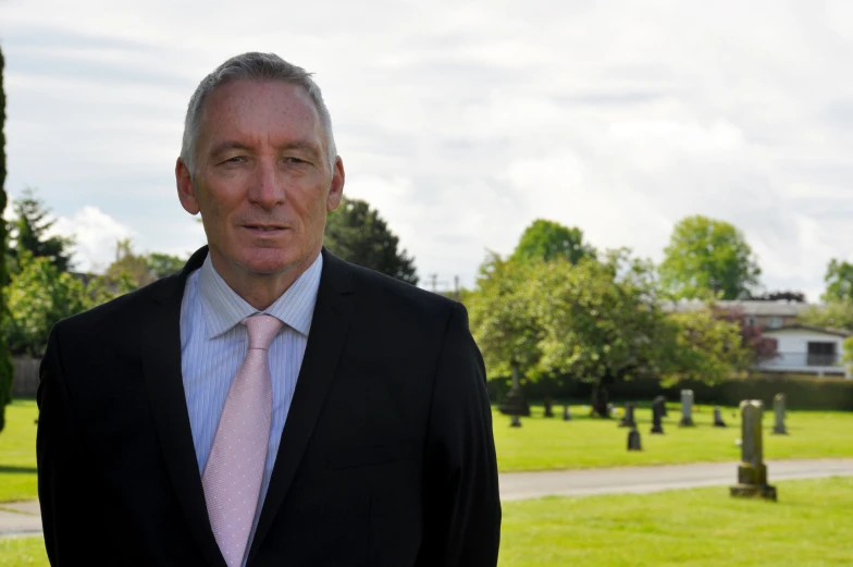 a man in a jacket and tie standing near a cemetery