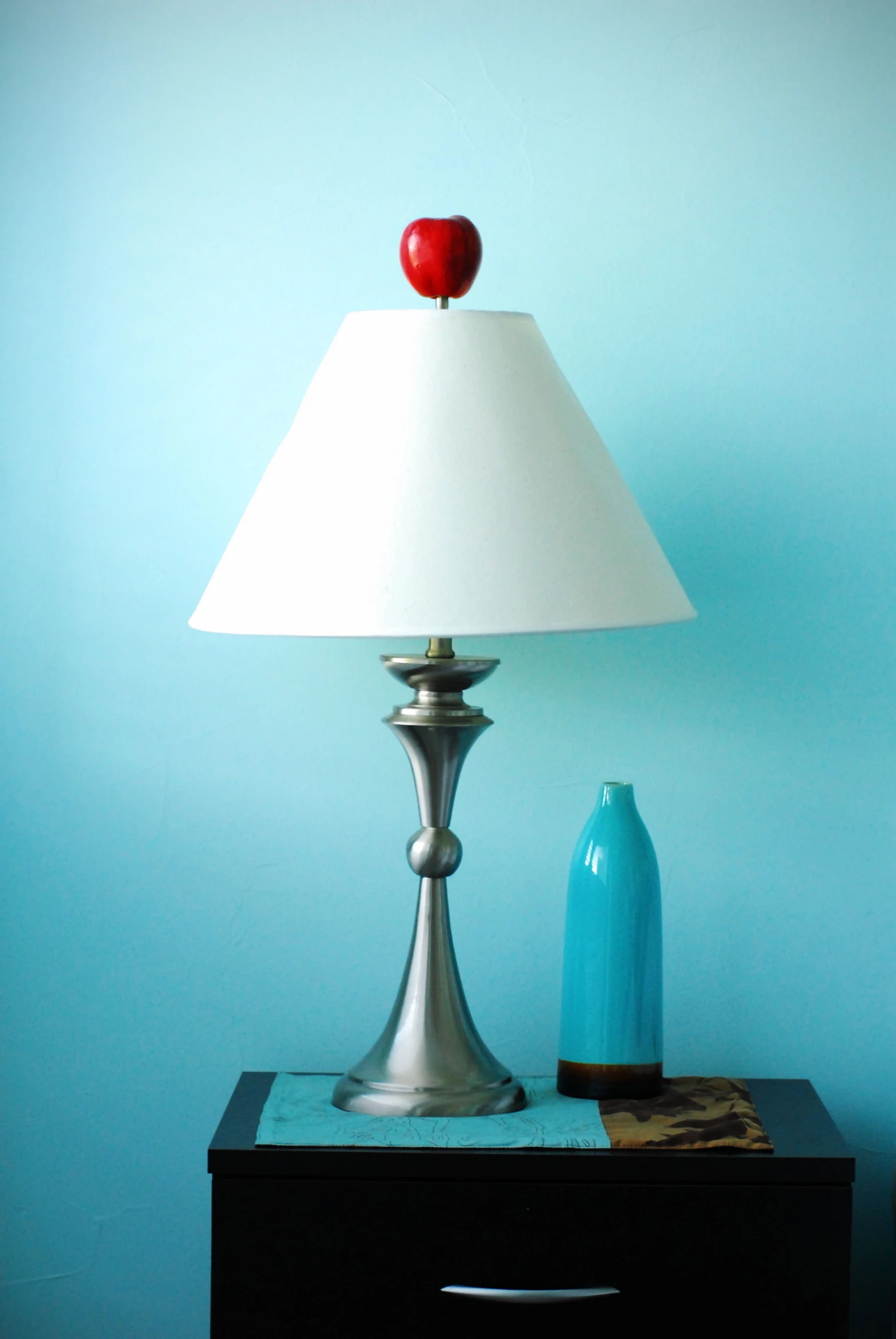 a light blue cabinet with a silver lamp and red apple on top