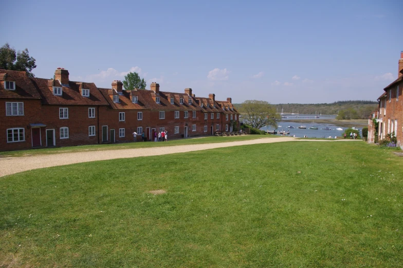 the old brick buildings along the edge of the river are near the edge of a field