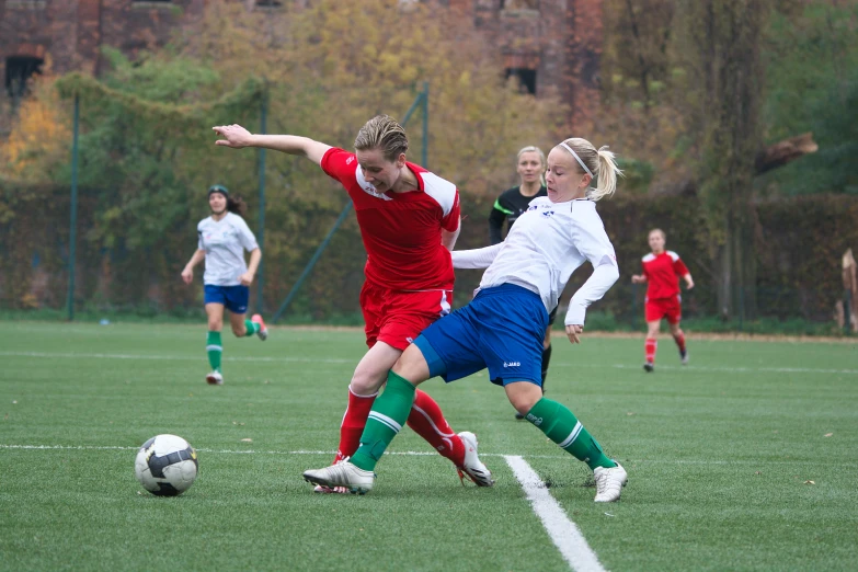 two girls are playing soccer, one is red and the other is blue