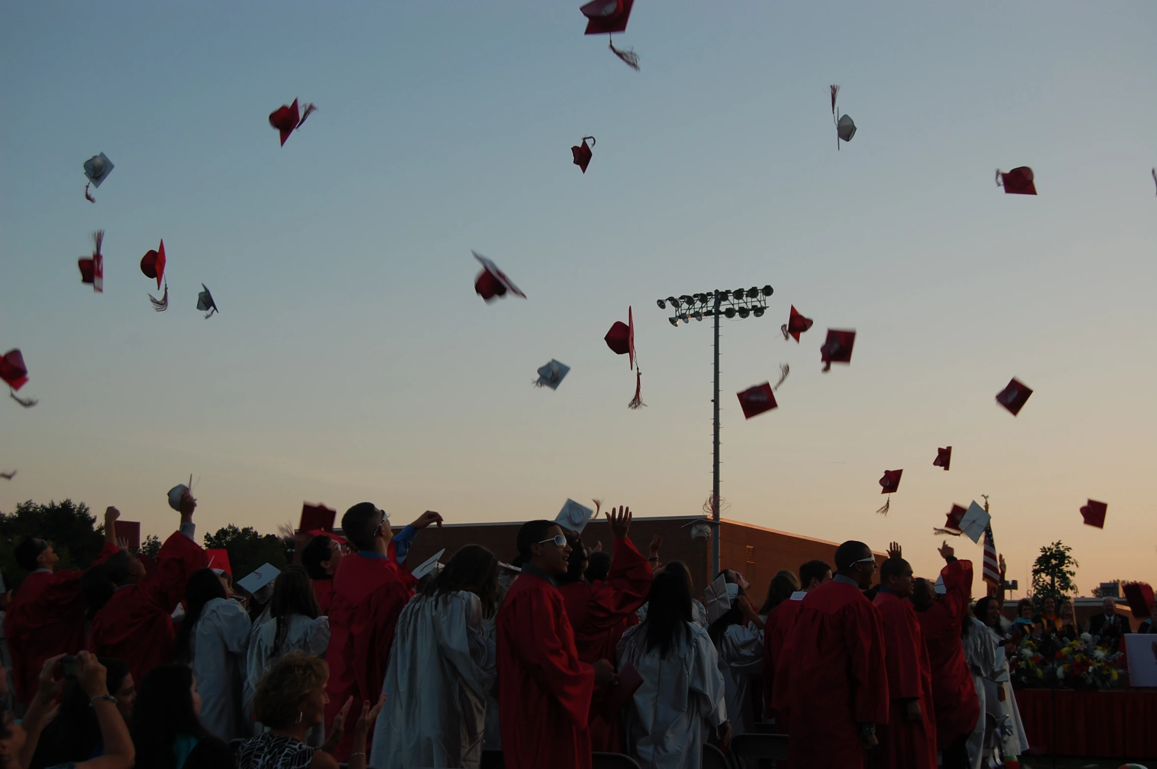 graduates in gowns and cap fly their caps at sunset