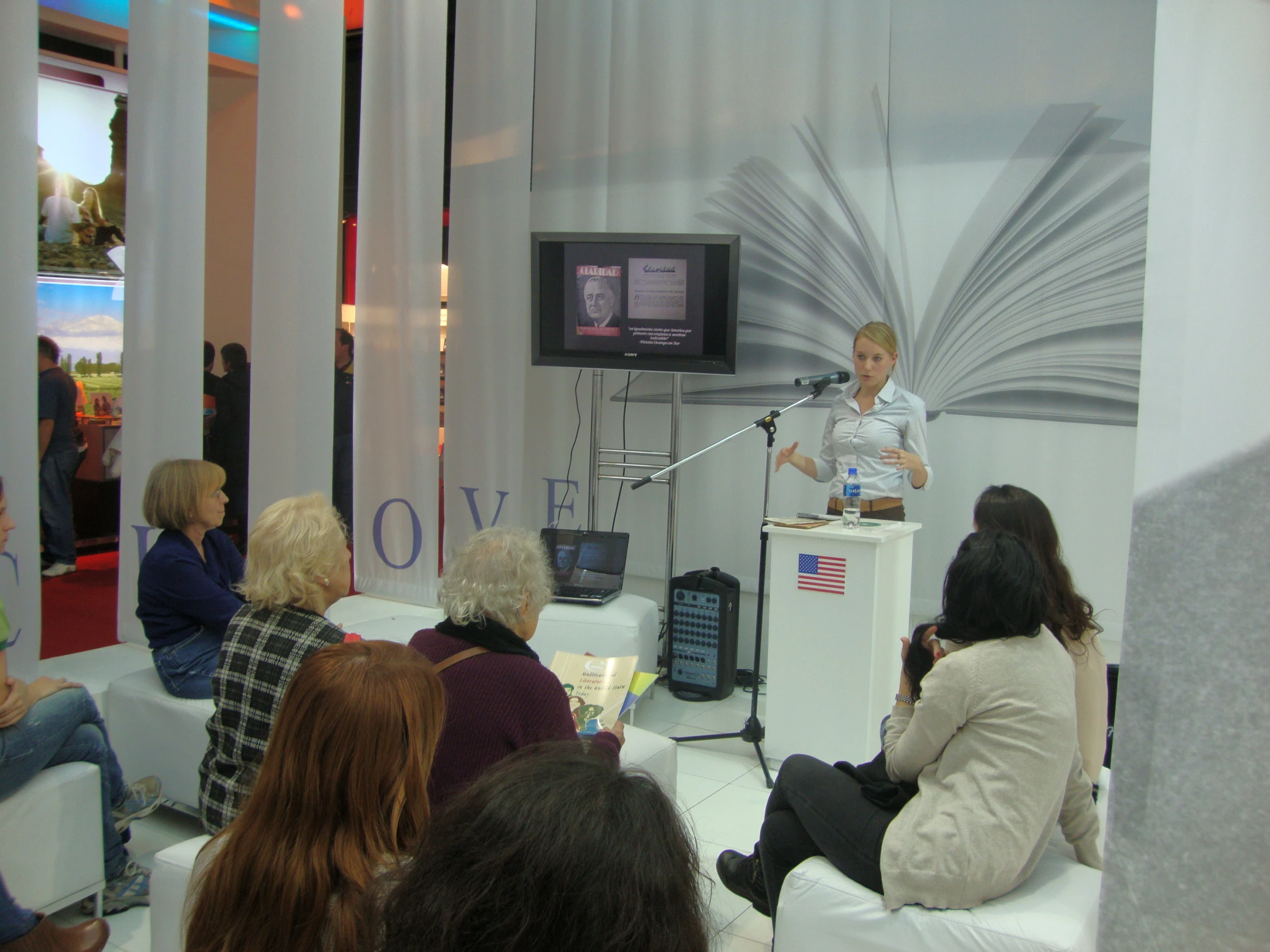 people sitting in chairs in front of a display with a man on the tv screen