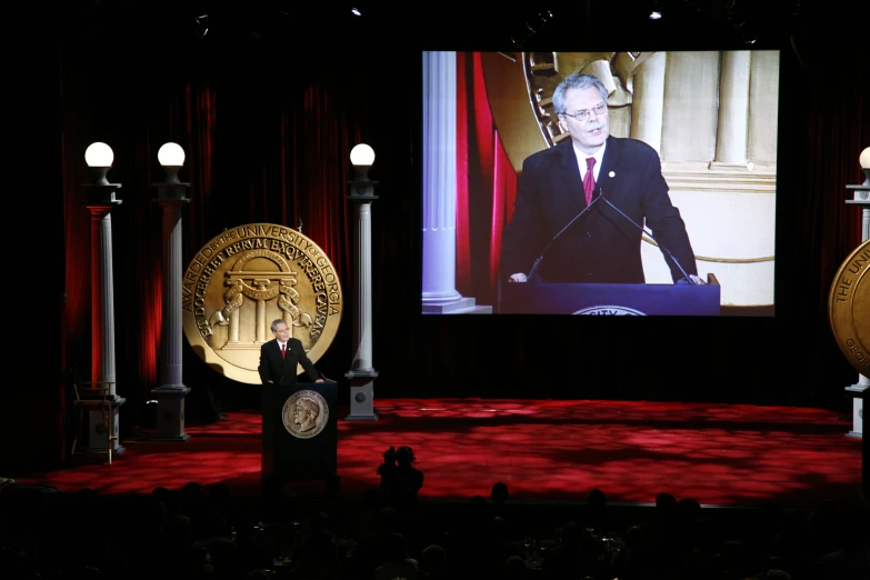 a man giving a speech in front of a video screen