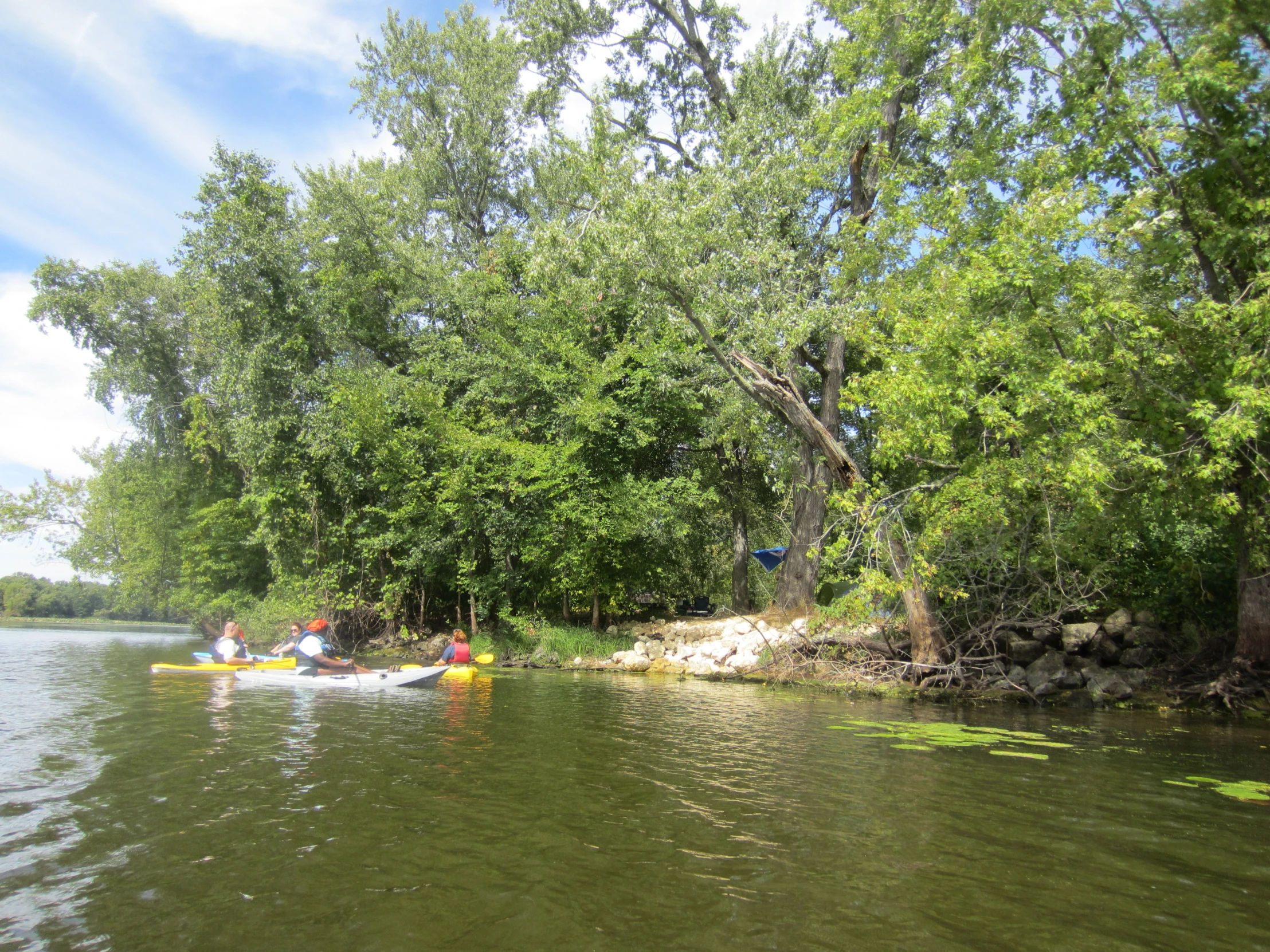 three people paddling on small boats down a river