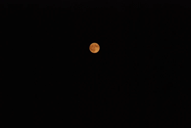 a picture taken from a telescope shows a bright orange moon rising in the night sky