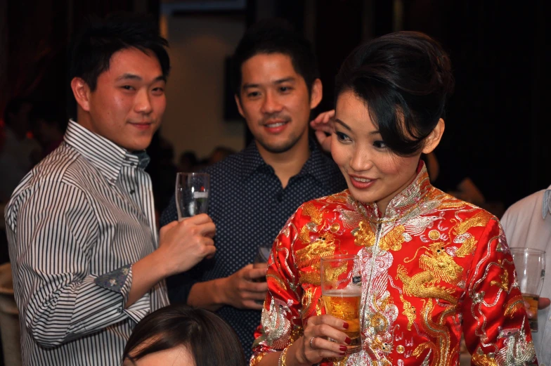 two asian women wearing a long red dress and a man in a striped shirt hold a glass of wine