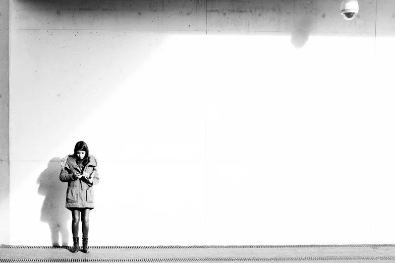 a woman in a coat is standing near a wall