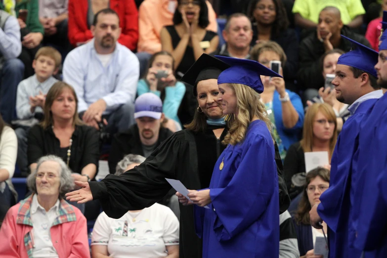 two women in graduation gowns are shaking hands with a graduate at commencement