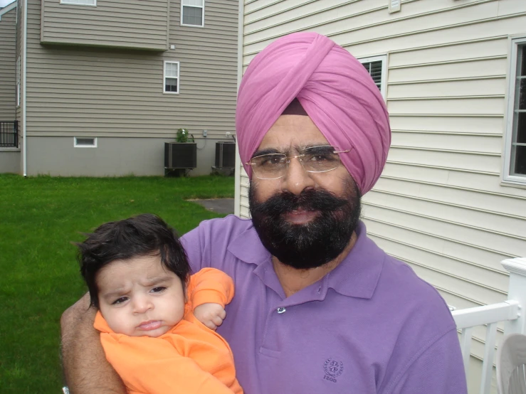 the man is holding his toddler, in a purple turban