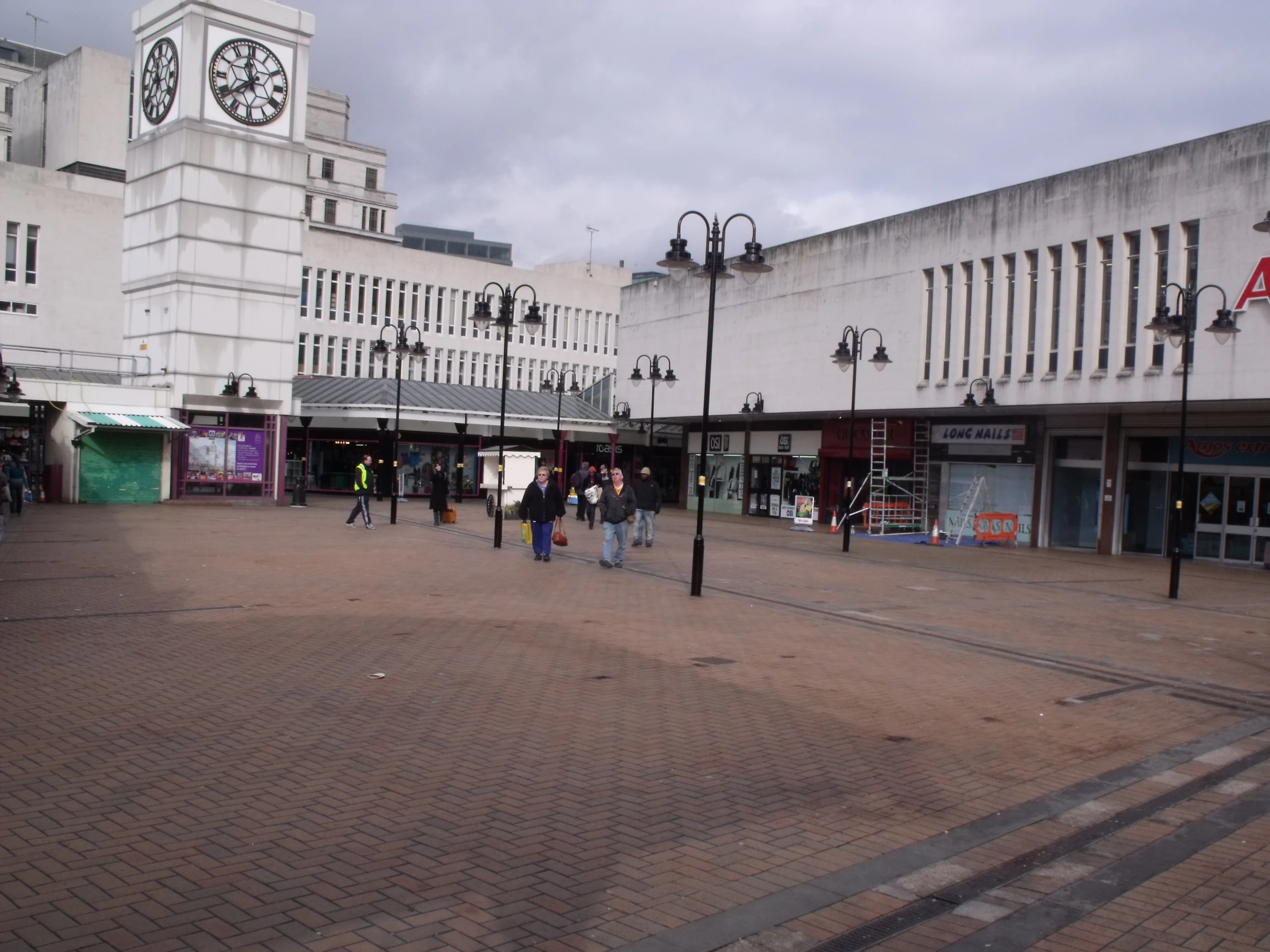 people walk through a square in front of a large building with a clock