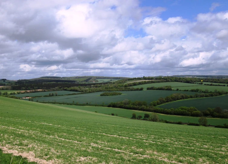 a lush green field surrounded by lots of clouds