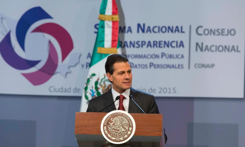 the man is speaking on stage with other flags behind him