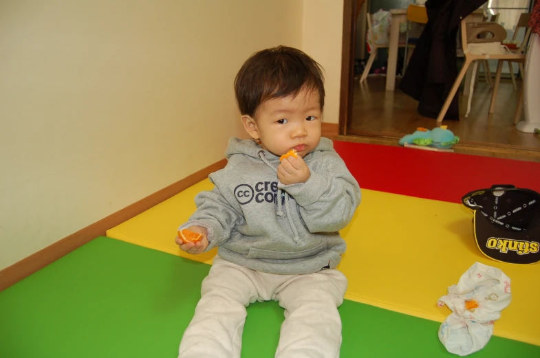 baby eating food while sitting on the floor in front of some things