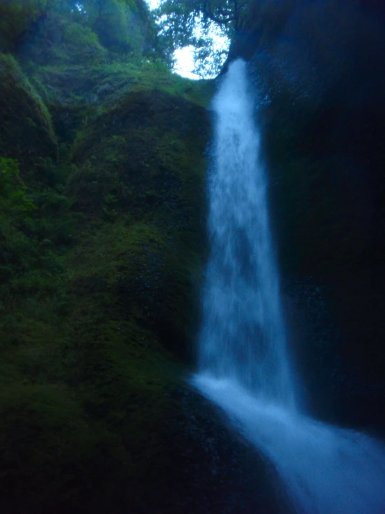 a large waterfall spouts down from a green hillside