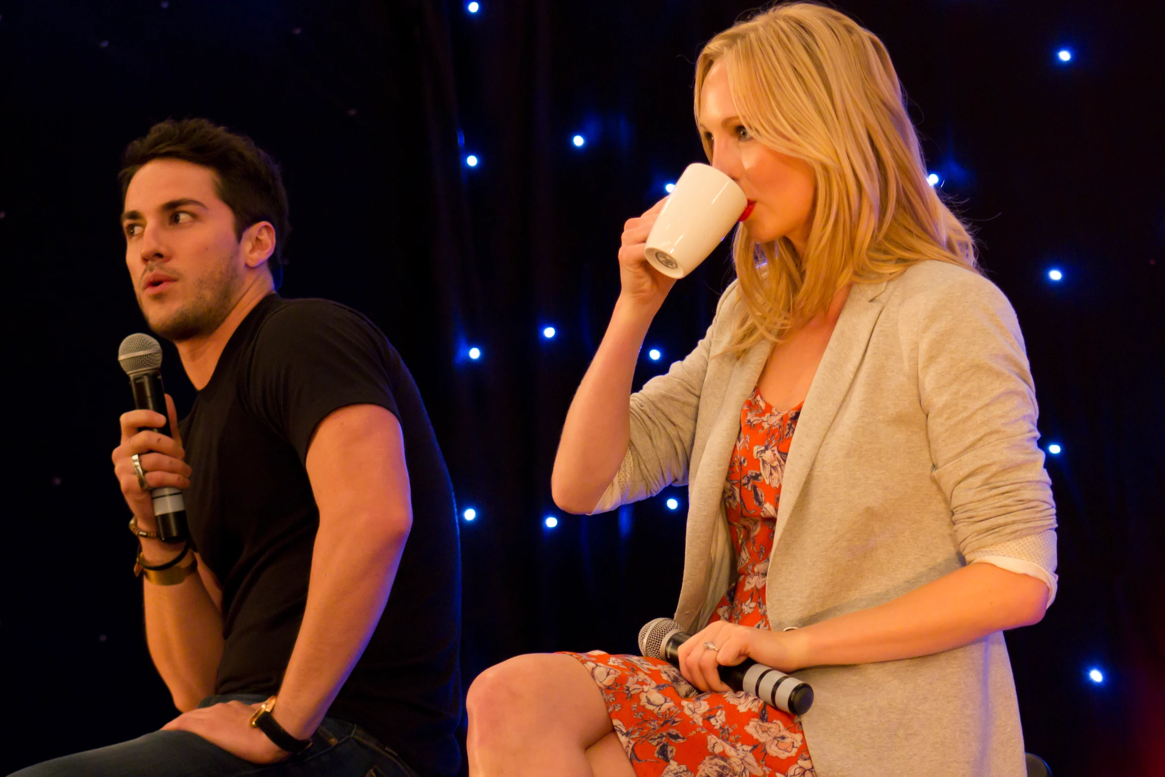 a young woman sitting down holding a mug next to a man