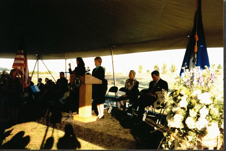 a group of people sitting under a tent while one woman holds a microphone