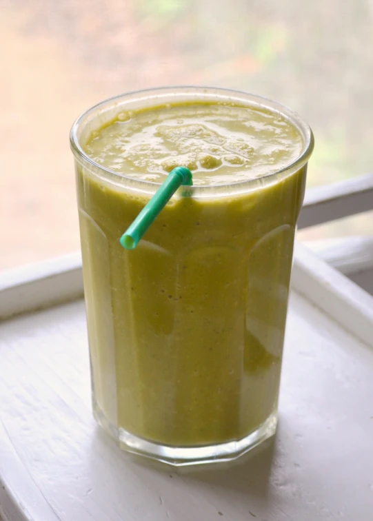 a green drink sitting on a windowsill with a blue straw in it