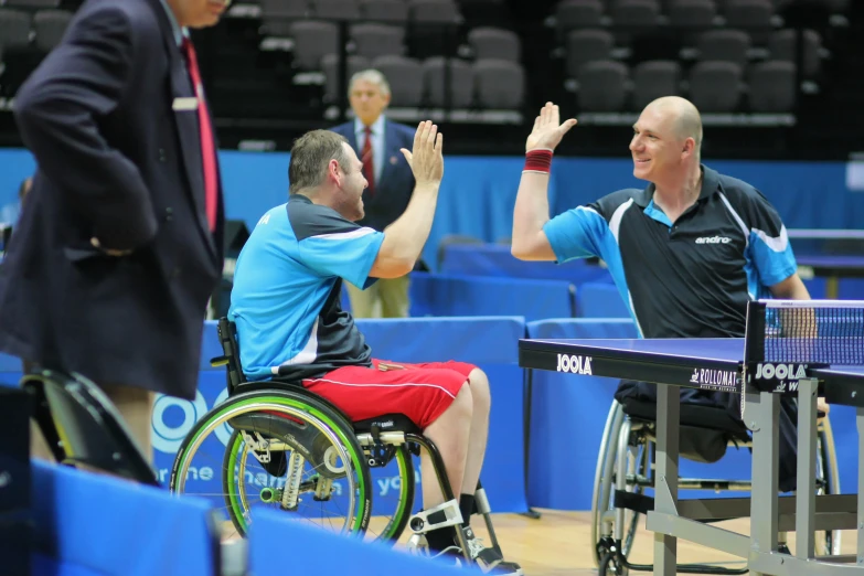 a person in a wheelchair greeting a player at an indoor competition