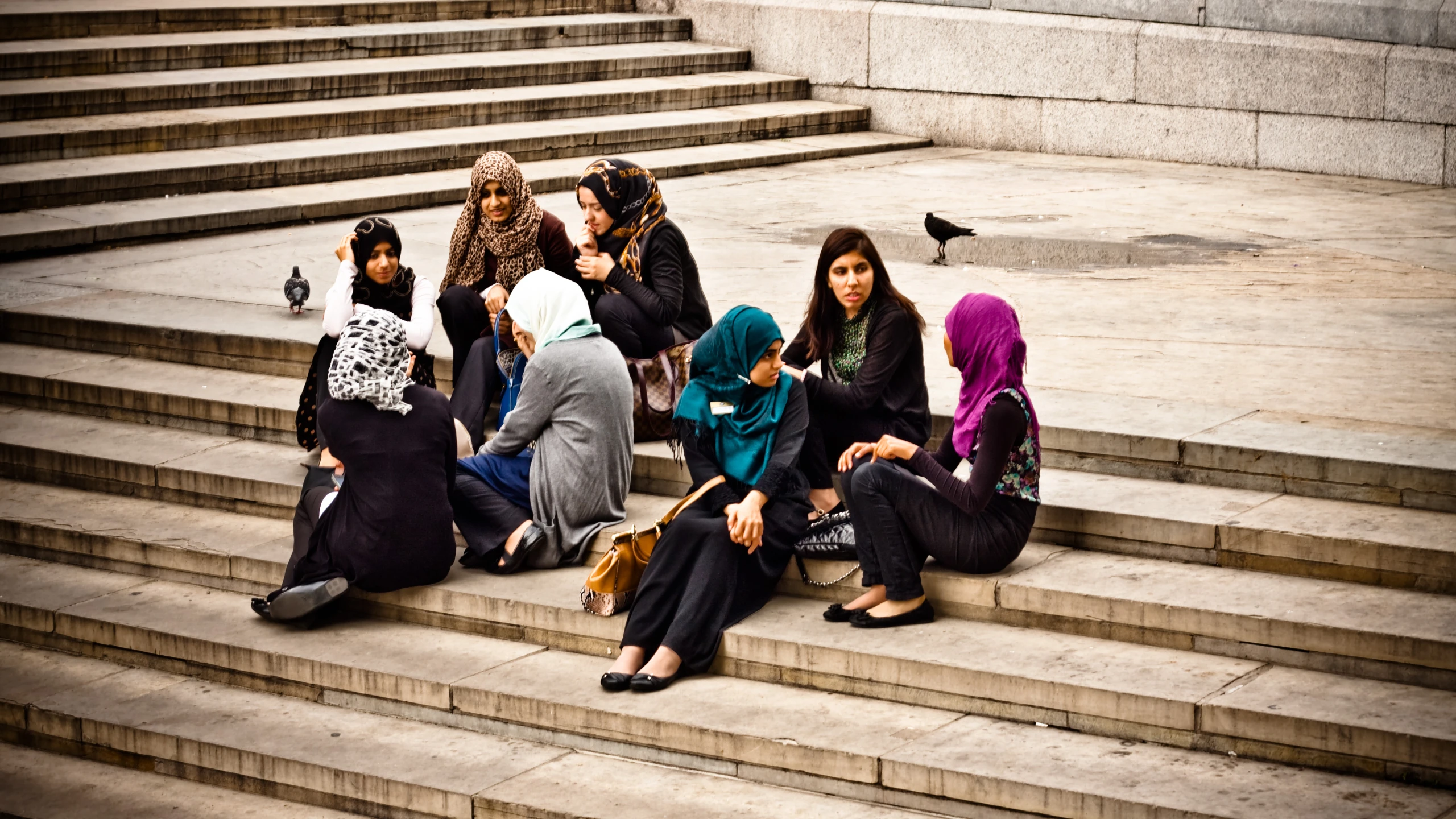 a group of young women sitting on steps next to a couple of pigeons