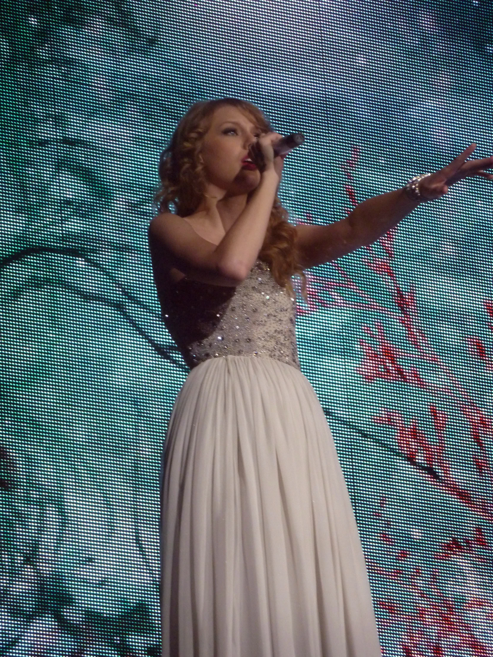 a young woman in a formal white dress sings on stage