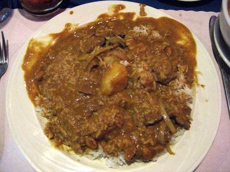 a picture of a plate of stew, rice and silverware on a table