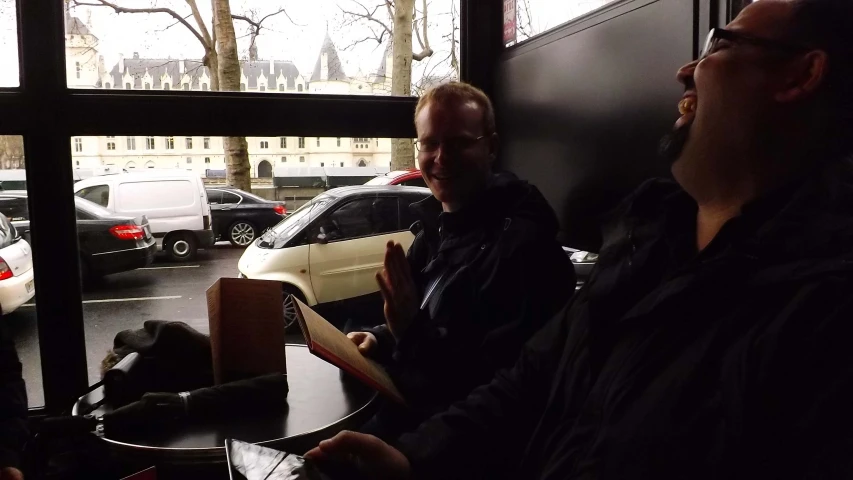 a man with his eyes closed sitting in a restaurant with another man