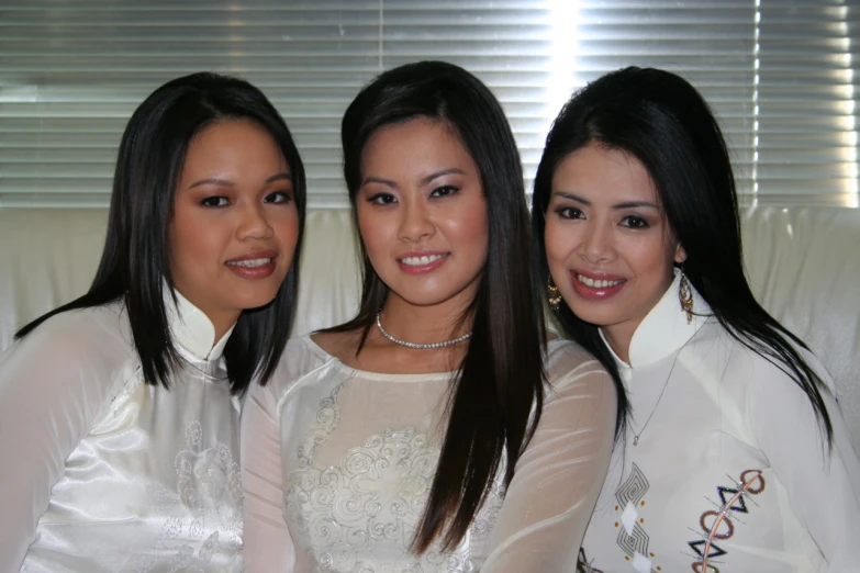 three women pose together with one dressed in a white suit and one with blue jeans