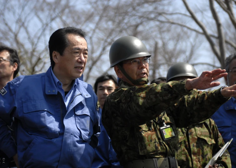 an asian man pointing with one hand and a soldier in the background