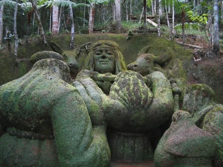 three statues in a wooded area with moss on them
