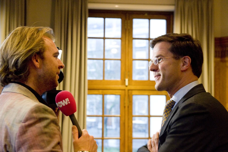 a man holding a microphone next to another person in a suit