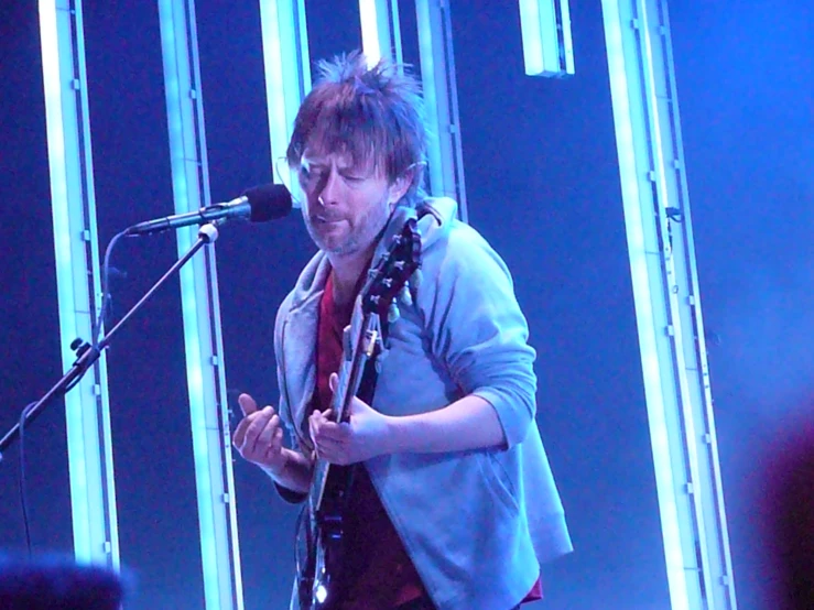 a man on stage holding an electric guitar in front of a microphone