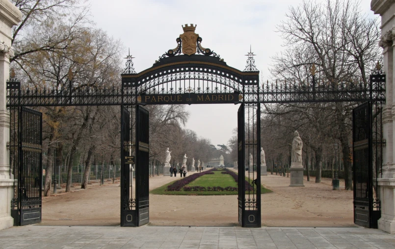 a gate with two statues, a monument and people in the distance