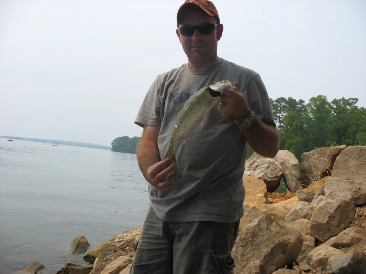 man in gray shirt holding a fish next to the water