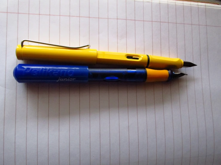 two pens laying on top of each other on top of a piece of paper